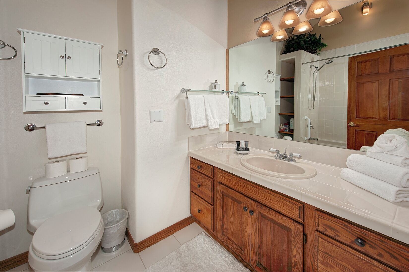 Une salle de bain comprenant des toilettes, un lavabo, un miroir et un meuble de rangement.