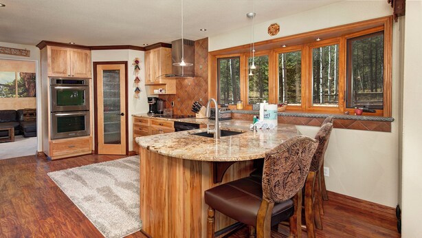 A kitchen with wooden cabinets, a built-in oven, a large window, and a bar area with a chair. - Mountain Home with Private Hot Tub (Silverthorne)