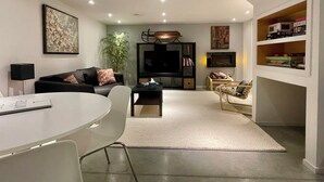 En moderne stue med sofa, fjernsyn, bogreol og et spiseområde med bord og stole.
