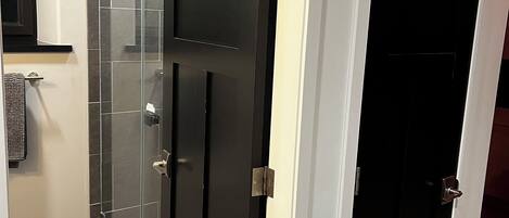 A modern bathroom with a glass shower enclosure, a black door, and a white wall.