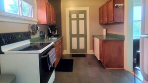 Una cucina compatta con fornello, forno e lavello. Si vede una porta con un'apertura sopra, e pensili in legno.