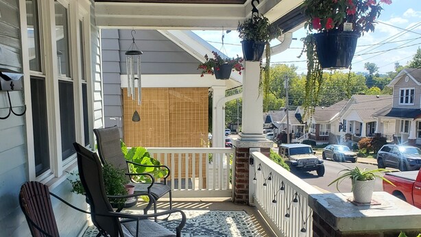 Un portico coperto con un tappeto decorato, due poltrone a dondolo e vasi di fiori pensili.