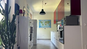 A kitchen with white cabinets, a map on the wall, and a potted plant. - Isa's Garden (Monterosso al Mare)