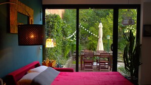 A bedroom with a large bed, a desk, and a chair, a window with curtains, and a view of greenery outside. - Isa's Garden (Monterosso al Mare)