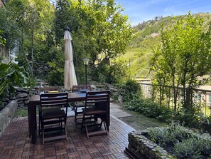 A patio with a table and chairs, surrounded by lush greenery and a stone wall. - Isa's Garden (Monterosso al Mare)