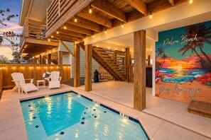 A pool area with a wooden deck, lounge chairs, and a mural of a beach scene. - Palm Beach! Ocean Views + Private Pool + Foosball! (Port Aransas)