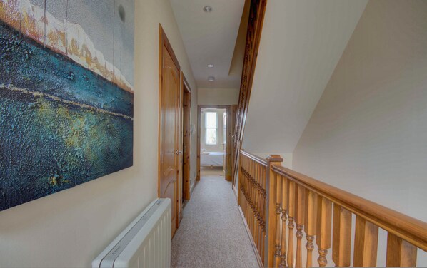 A hallway with a radiator, wooden doors, a staircase with a wooden handrail, and a large abstract painting on the wall.