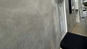 Un edificio con facciata grigia, un tappetino d'ingresso nero e una piccola finestra con cornice bianca.