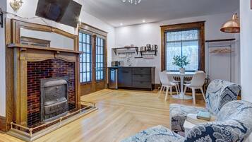 Ein modernes Wohnzimmer mit Kamin, einem Essbereich mit Tisch und Stühlen sowie einer Küchenzeile mit Geräten und Regalen.