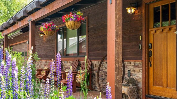 Una cabaña de madera con macetas colgantes de flores, una chimenea de piedra y una puerta de madera.
