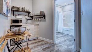 Eine moderne Küche mit einem Holztisch, einer großen Schüssel und verschiedenen Geräten. Eine Glastür führt zu einem Badezimmer.