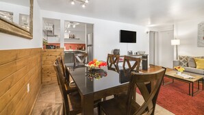 A modern kitchen with white cabinets, a dining area with a glass table, and a living room with a sofa and a TV. - RMR: Tensleep B4 Condo in Teton Village (Teton Village)