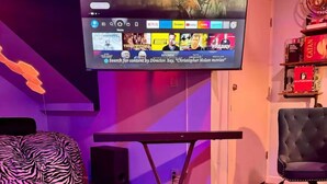 En moderne stue med et vægmonteret TV der viser en film, en sofa med zebramønster, et glas sofabord og en sort læderstol.