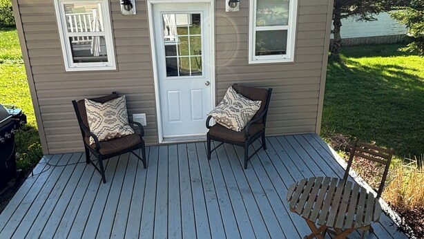 A small cabin with a deck, two chairs, a table, and a door.