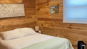 A wooden-paneled room with a bed, a radiator, and a window with blinds.