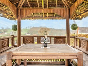 A wooden gazebo with a table set for two, featuring a bottle of champagne and a wine glass. - 5 bedroom accommodation in Drybrook (Drybrook)