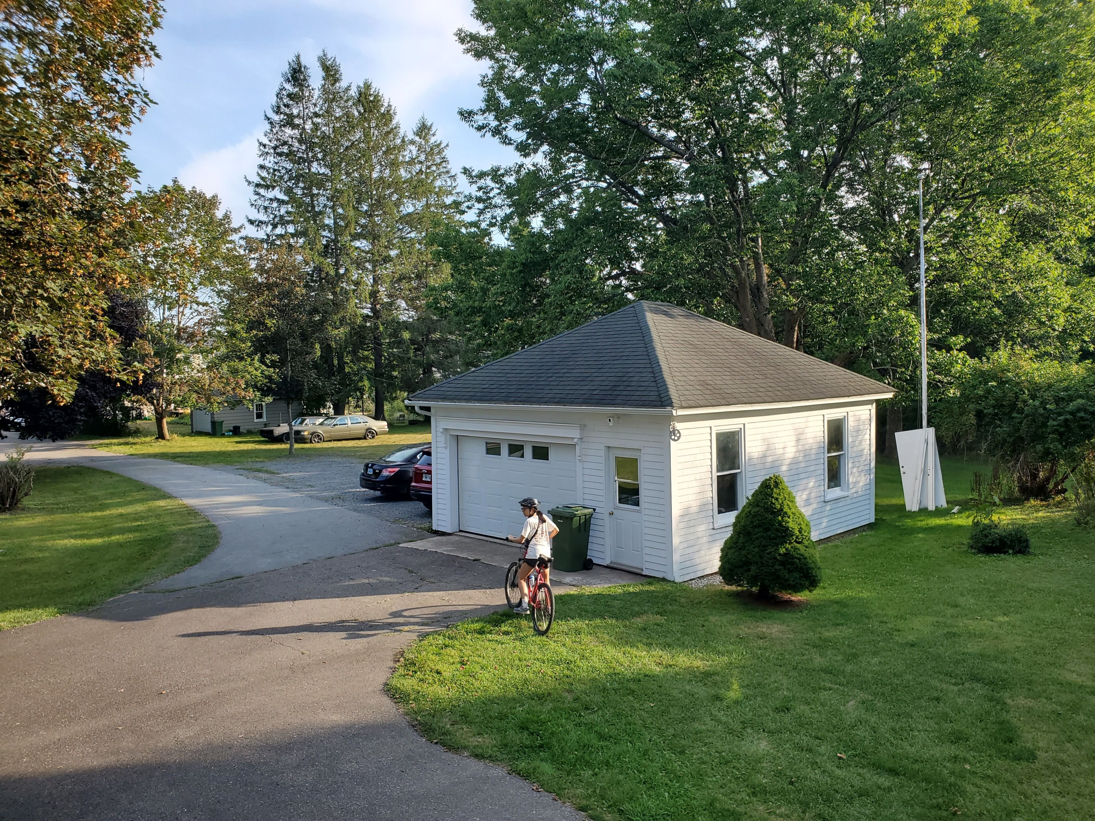Zona residencial con una pequeña casa blanca, un camino de entrada pavimentado y un ciclista.