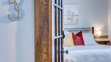 A hotel room with a wooden door, a bed with white bedding, and a number '3' sign on the wall.