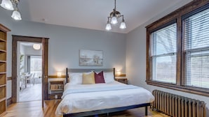 Une chambre à coucher avec un lit, des lampes de chevet, un radiateur et une fenêtre avec des stores.
