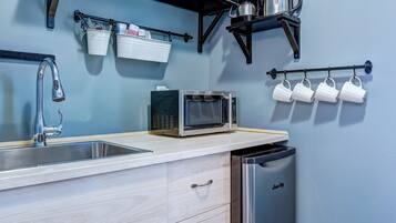 Une cuisine moderne équipée d’un évier, d’un four à micro-ondes et d’un lave-vaisselle. Des étagères au-dessus du plan de travail servent à ranger les verres et les tasses.