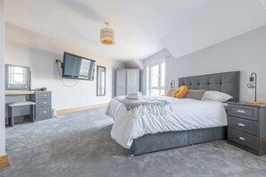 Un dormitorio con cama, mesitas de noche, escritorio, televisor y ventana.