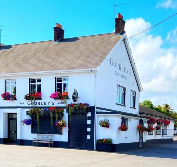 A white building with the sign 'Gourley's Bar-Venue' and flower baskets on the windowsills.