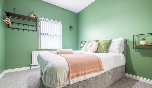 A bedroom with a bed, a radiator, a window with blinds, a shelf with a plant, and a wall-mounted plant. - 3BR House, Central, Pet Friendly, Next to Café (Ballycastle)
