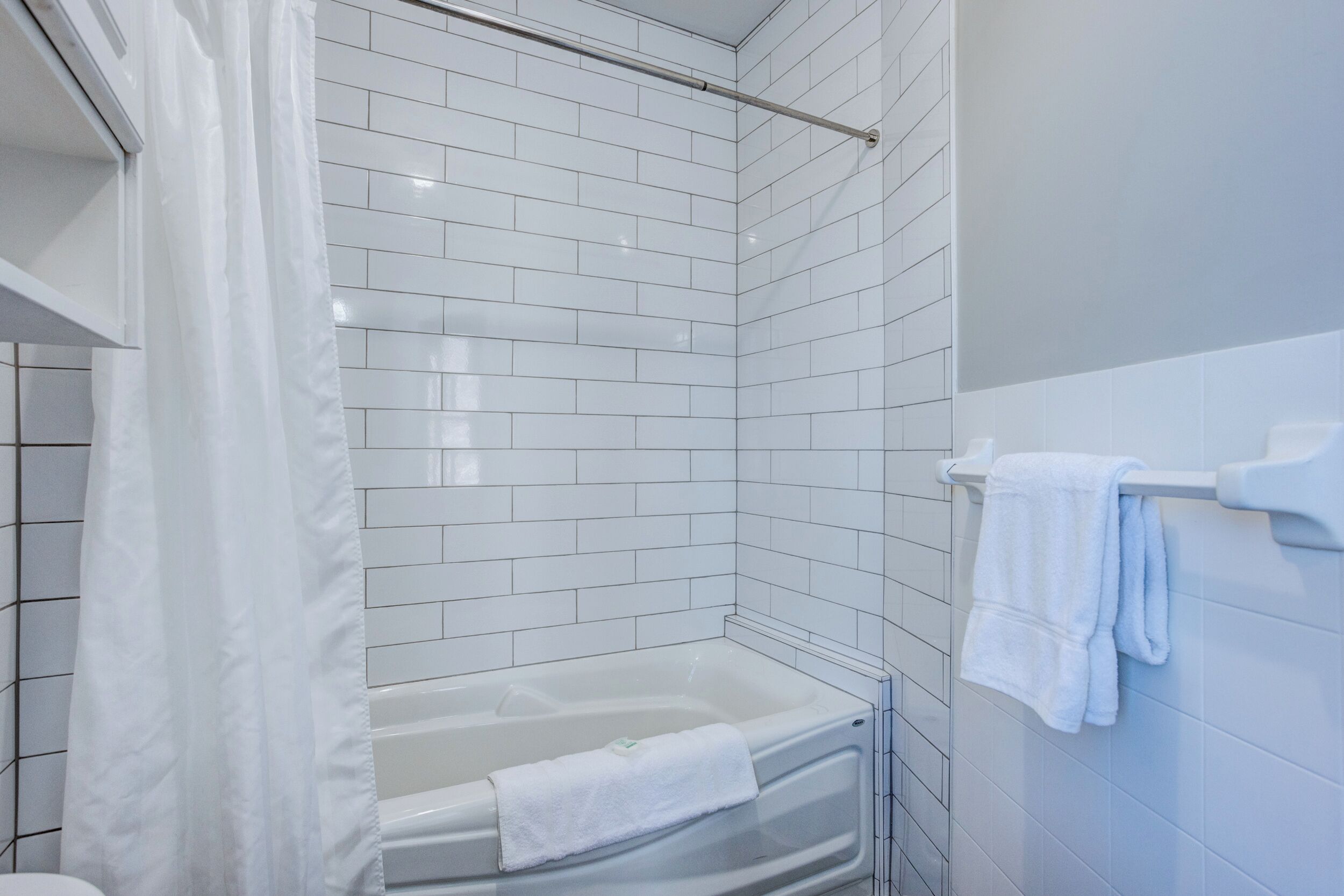 A modern bathroom with white tiled walls, a glass shower enclosure, and a bathtub with a towel.
