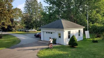 A residential area with a small white house, a paved driveway, and a cyclist.