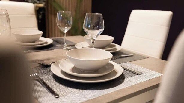 Une table à manger dress ée avec de l’assiette, des bols et des couverts blancs, et un set de table placé en dessous.