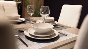 A dining table set with white plates, bowls, and cutlery, with a placemat underneath. - 3BR Pet-Friendly Coastal House Ballycastle (Ballycastle)