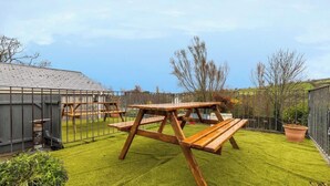 Un espace extérieur clôturé, avec une table de pique-nique en bois et un abri de jardin.