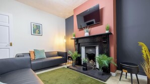 Un salon avec un canapé, une cheminée, un téléviseur et des plantes en pot.