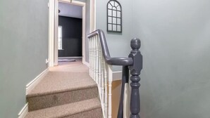 Un escalier dont les marches sont recouvertes de moquette, avec une main courante blanche et une balustrade de couleur foncée.