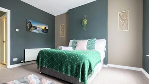 Une chambre avec un lit, un radiateur, un tableau accroché au mur et une plante suspendue.