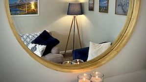 A round mirror reflecting a room with a floor lamp, a sofa with patterned cushions, and wall-mounted artwork. - Quiet 2BR Home with Garden, Sleeps 5 (Londonderry)