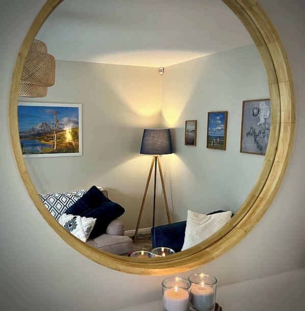 Un miroir rond reflétant une pièce avec un lampadaire, un canapé orné de coussins à motifs et des œuvres d’art accrochées au mur.