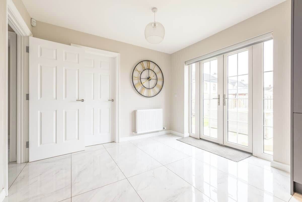 A spacious room with a large white door, a radiator, a wall clock, and a large window with a view.