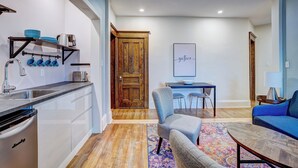 A modern kitchen with a dishwasher, a wooden door, a dining area with a table and chairs, and a blue sofa. - Executive 1-Bedroom King Bed Suite in Lunenburg (Suite 5) (Lunenburg)