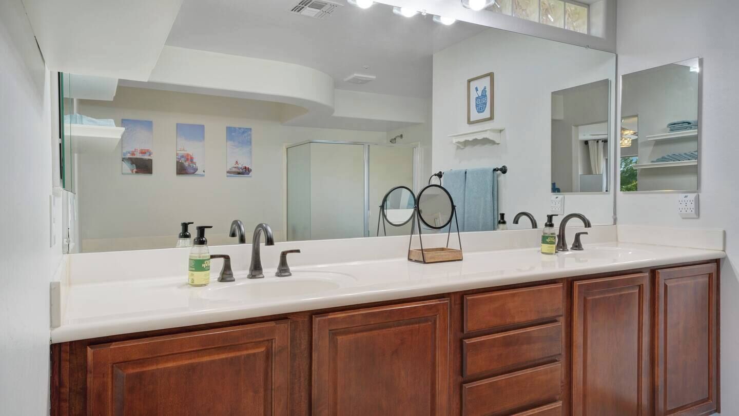 A bathroom with a large mirror, two sinks, wooden cabinets, and a towel rack.
