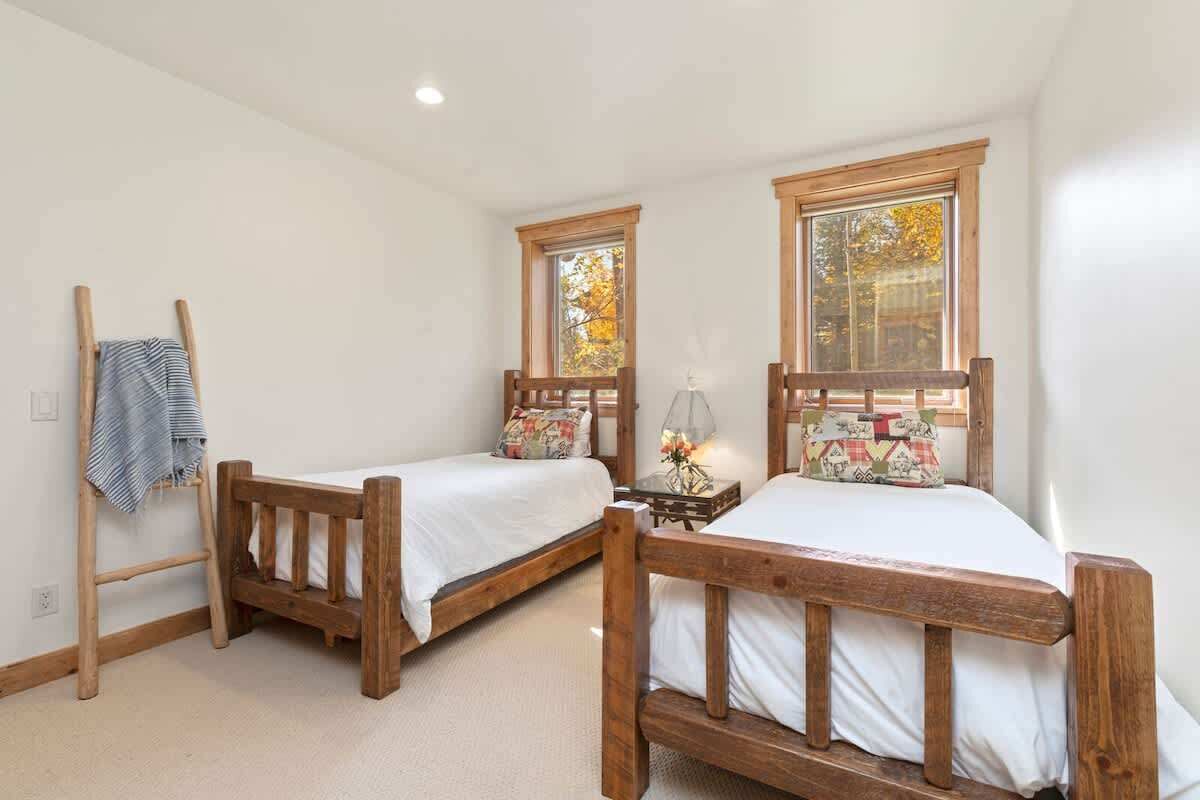 A bedroom with two wooden beds, a ladder, and a window with autumn leaves.