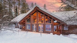 Een houten chalet met grote ramen, omgeven door met sneeuw bedekte bomen.