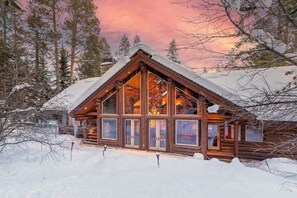 A log cabin with large windows, surrounded by snow-covered trees.