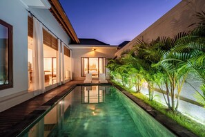 Un'area piscina moderna con piscina cristallina, solarium in legno e vegetazione rigogliosa.