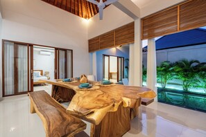 Una stanza spaziosa con un grande tavolo da pranzo in legno, panche e vista su un giardino tropicale.