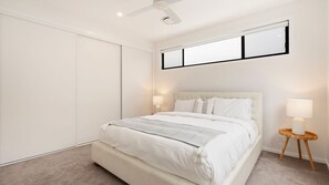 Een slaapkamer met een bed, een plafondventilator, een nachtkastje met een lamp en een raam met jaloezieën.