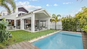 Een modern huis met een zwembad, een overdekt terras en een verzorgd gazon.