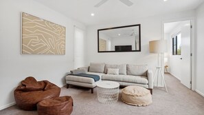 Una sala de estar moderna con un sofá, una mesa de centro, un sillón de peluche, una lámpara de pie y un cuadro abstracto grande.
