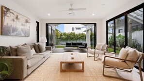 Una sala de estar moderna con un sofá, sillas, una mesa de centro y un ventanal que ofrece vistas a un jardín.