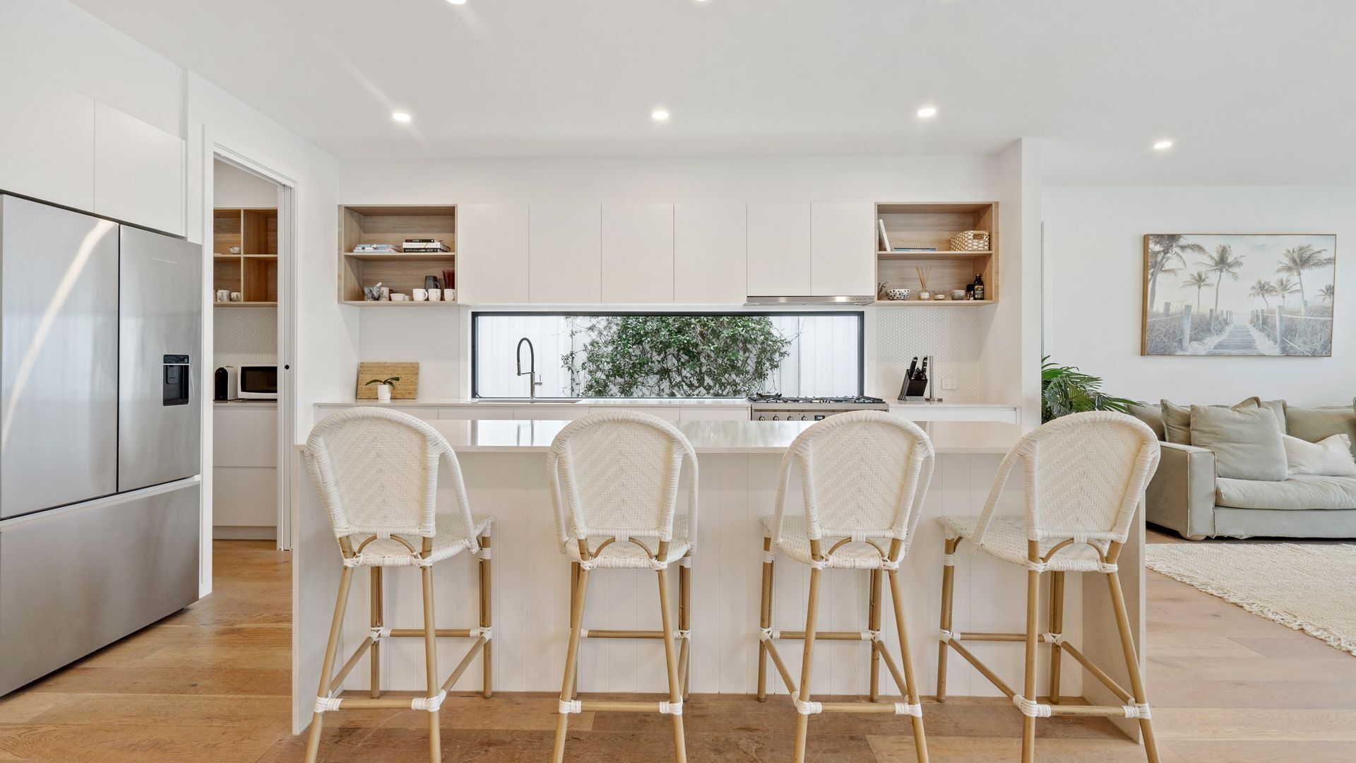 A modern kitchen with a central island, white cabinetry, and a dining area with four wicker chairs.